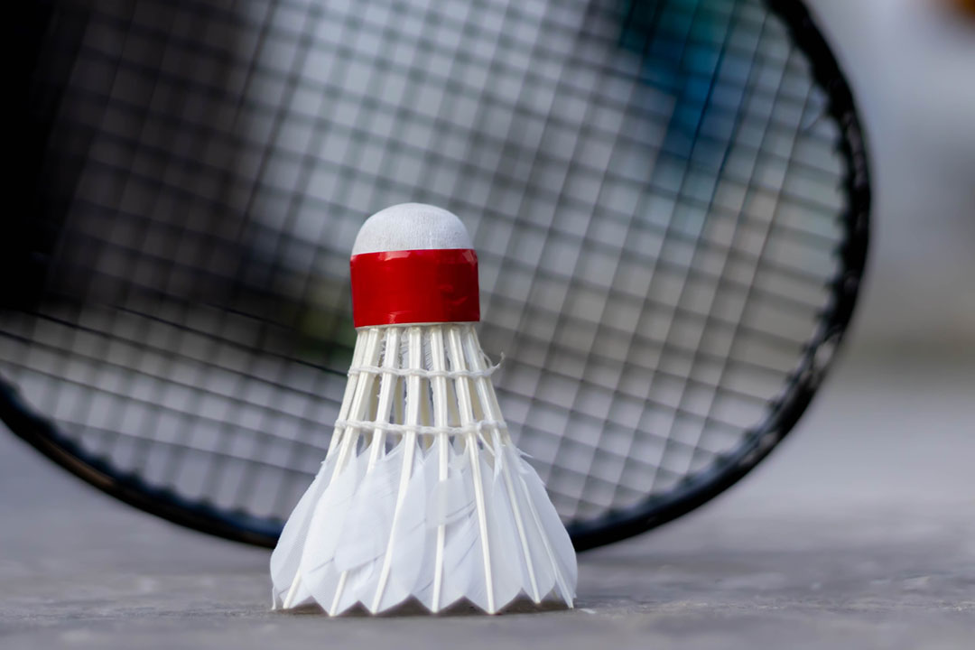 Blurred Badmington racket in background and shuttlecock, in focus in the foreground